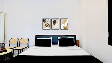Habitación de hotel con cama, dos sillas, una mesa y tres cuadros enmarcados en la pared.