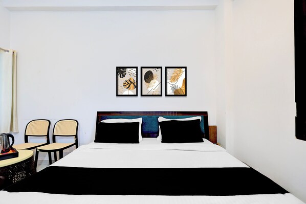 A hotel room with a bed, two chairs, a table, and three framed artworks on the wall.