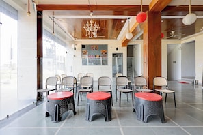 A spacious indoor area with multiple seating arrangements, including chairs and tables, and a large window providing natural light.