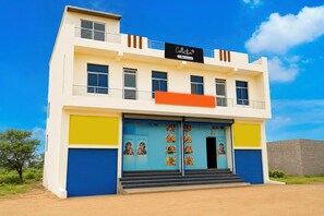A two-story building with a flat roof, a balcony on the upper floor, and a large blue door with colorful artwork.