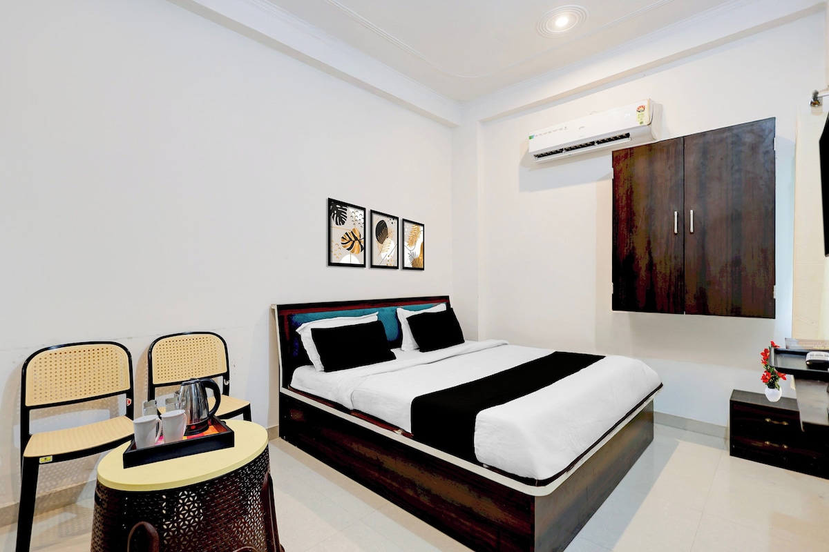 A modern bedroom with a bed, two chairs, a small table, an air conditioning unit, and artwork on the wall.