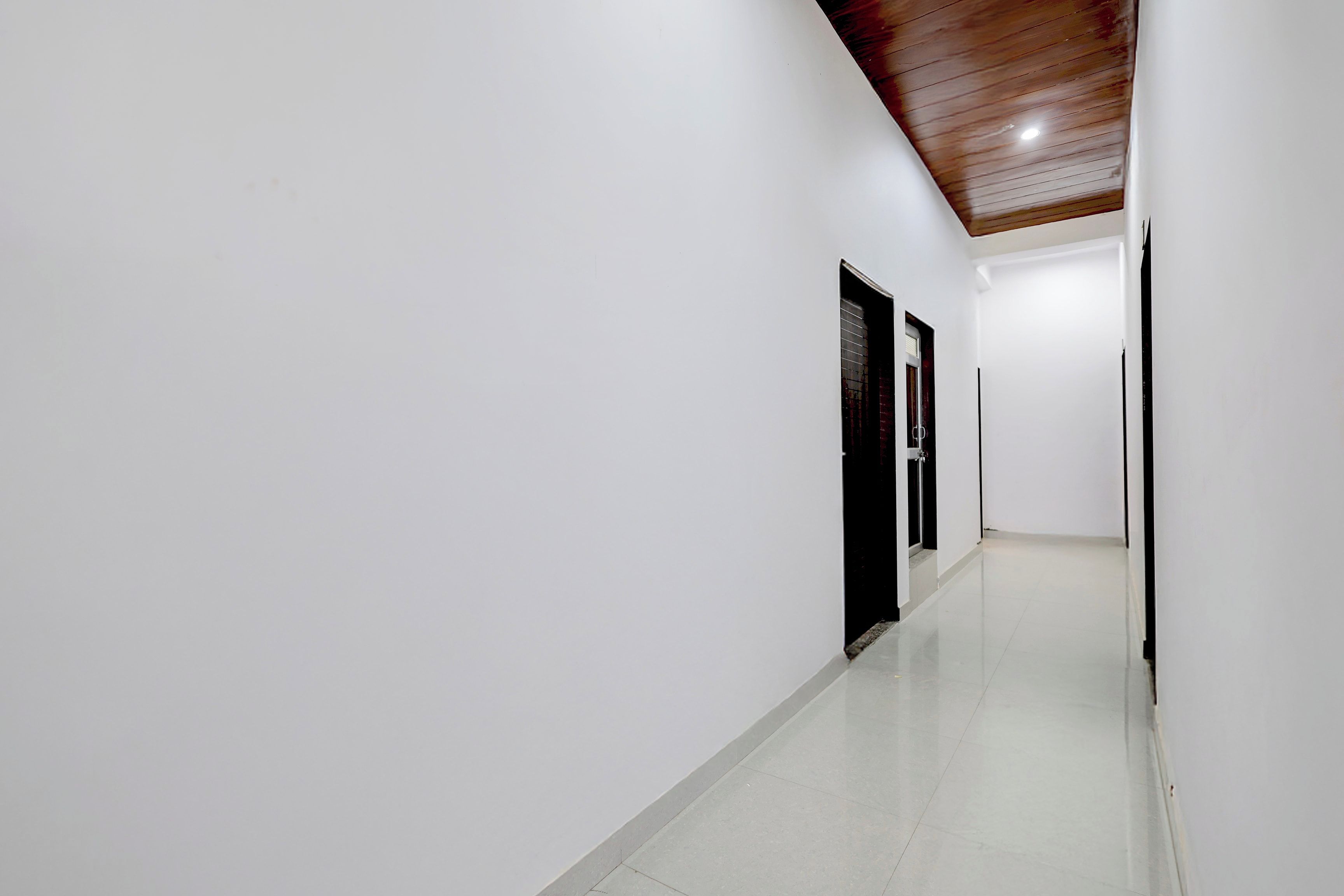 A corridor with white walls and a wooden ceiling, leading to a door with a window.