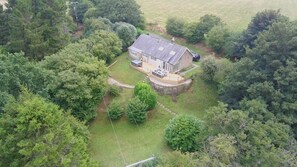 A house with a stone foundation, surrounded by dense greenery and a clear sky. - Hedley Dene Cottage (Morpeth)