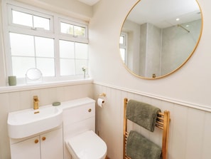 A bathroom with a white vanity, a toilet, a towel rack, and a round mirror. - Hedley Dene Cottage (Morpeth)