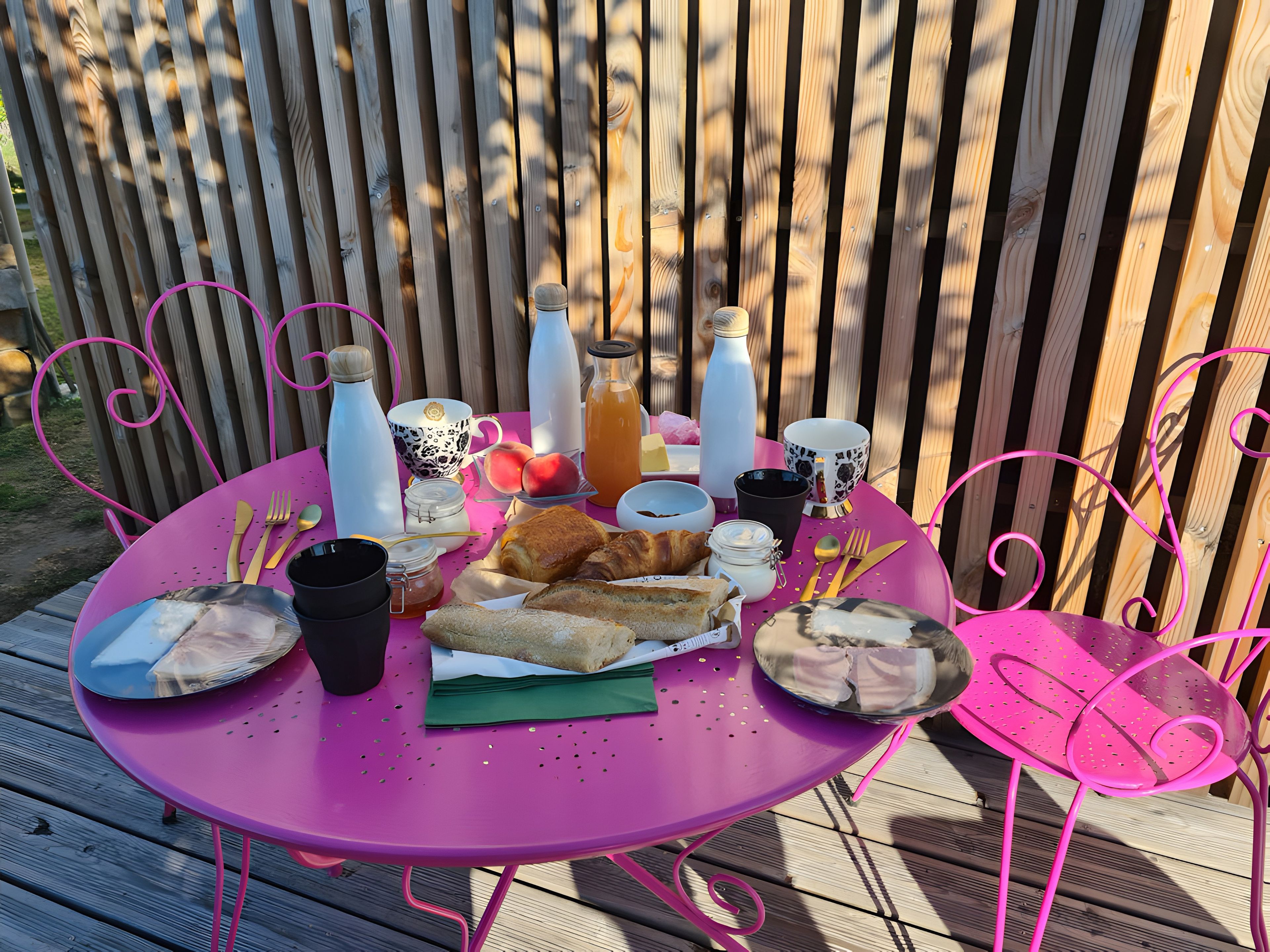 Een ronde tafel met een roze tafelkleed, omringd door roze stoelen, buiten opstelling met een houten hek op de achtergrond.