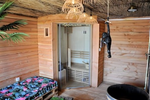 A wooden room with a glass door leading to a bathroom, a hanging monkey decoration, and a bed with a floral bedspread.
