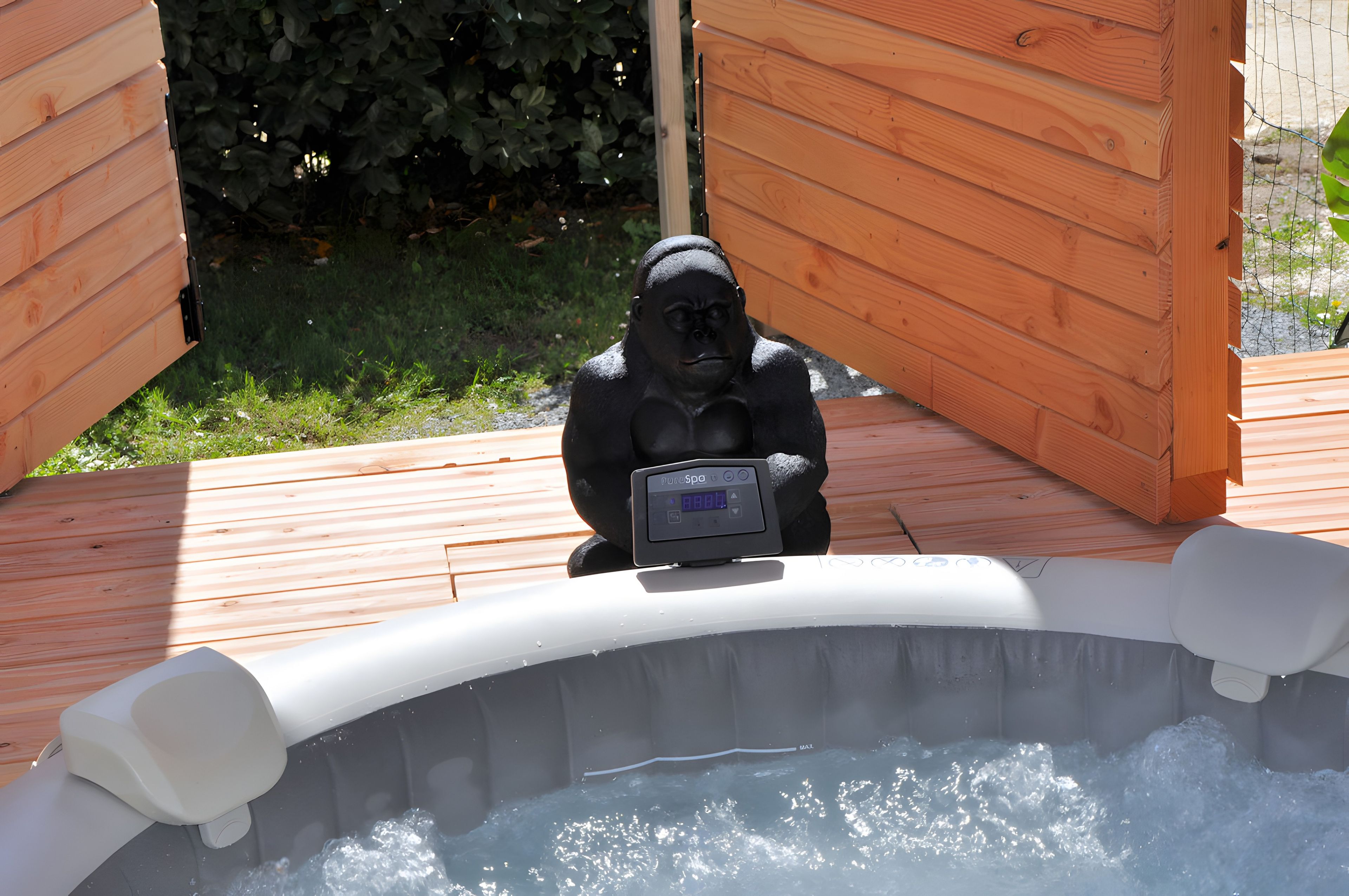 A hot tub with a gorilla statue in the center, surrounded by wooden deck and greenery.