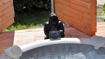 A hot tub with a gorilla statue in the center, surrounded by wooden deck and greenery.