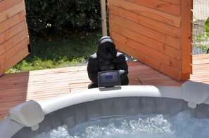 A hot tub with a gorilla statue in the center, surrounded by wooden deck and greenery.