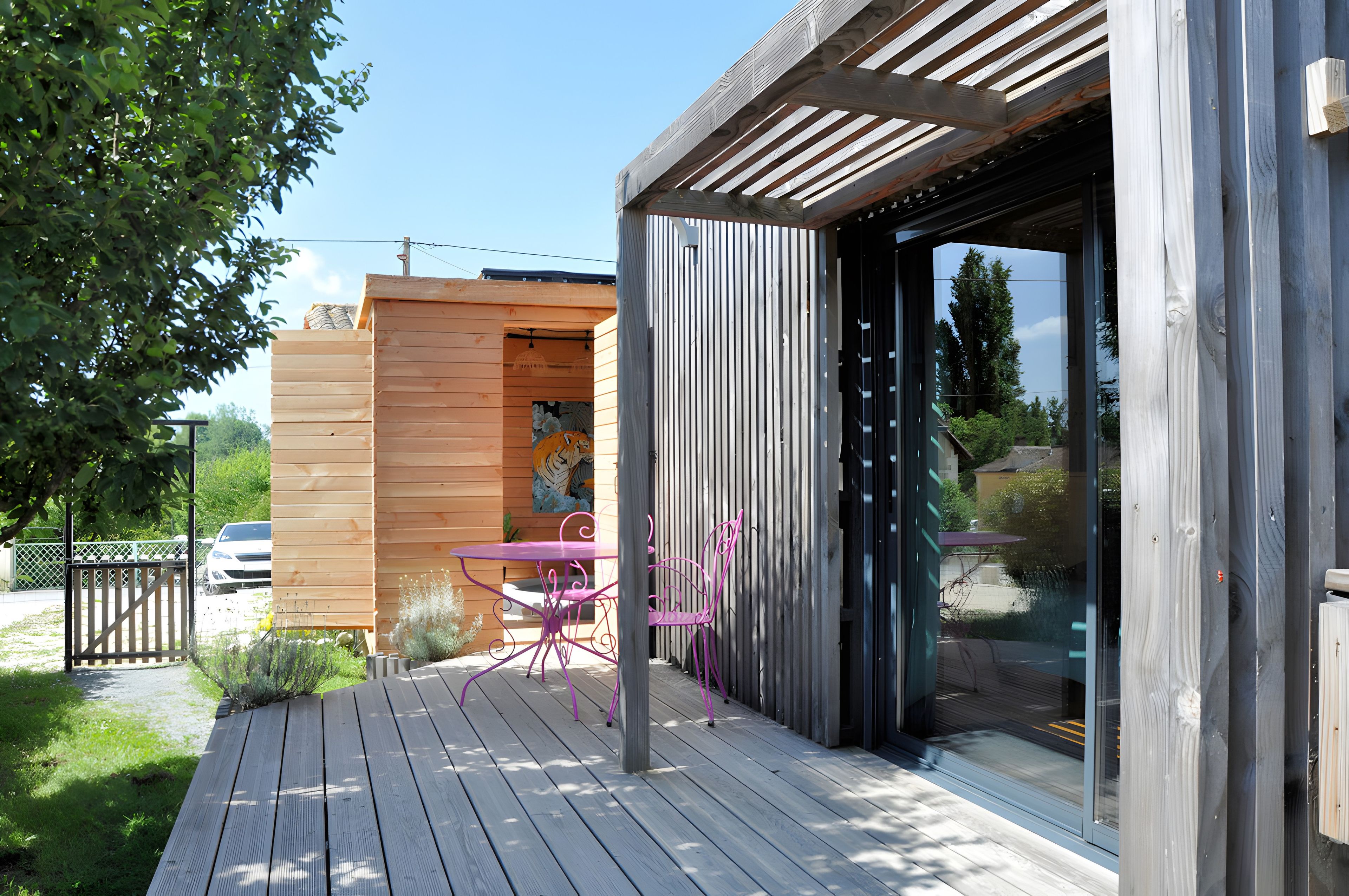 Een houten terras met een tafel, stoelen, een glazen toegang en uitzicht op de omliggende begroeiing.
