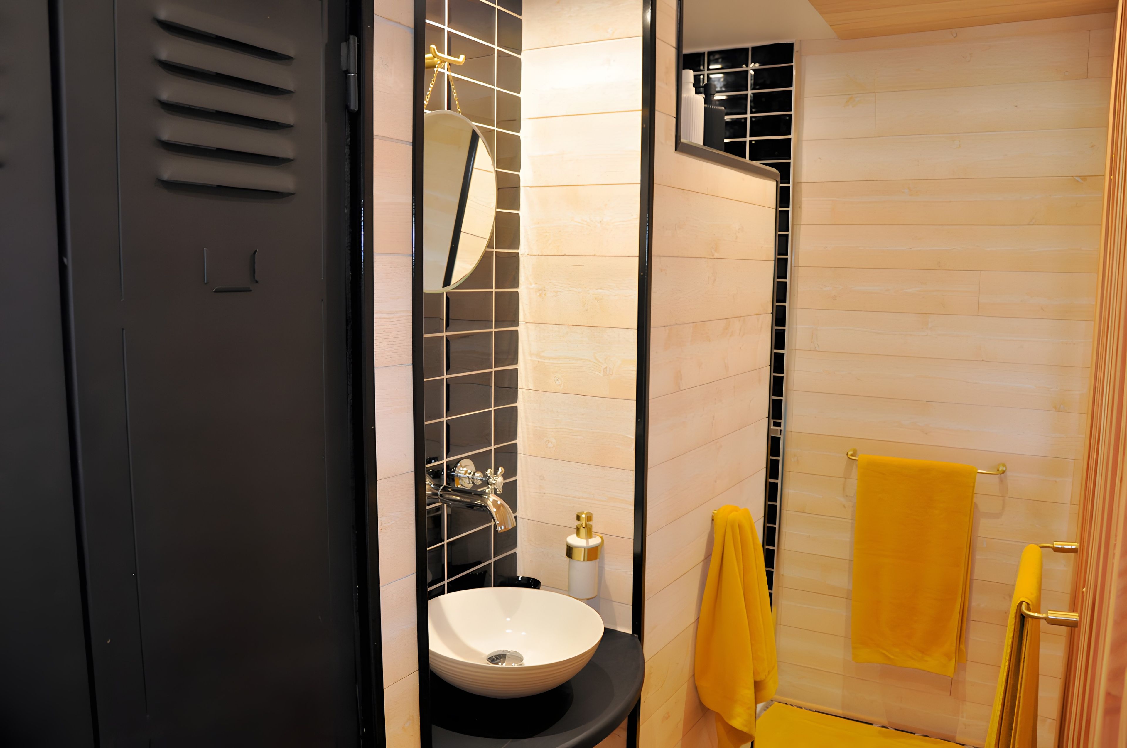 Un baño con una puerta negra, un lavabo blanco, un espejo y una toalla amarilla.