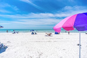 En strand med hvidt sand, klarblå himmel og nogle få parasoller.
