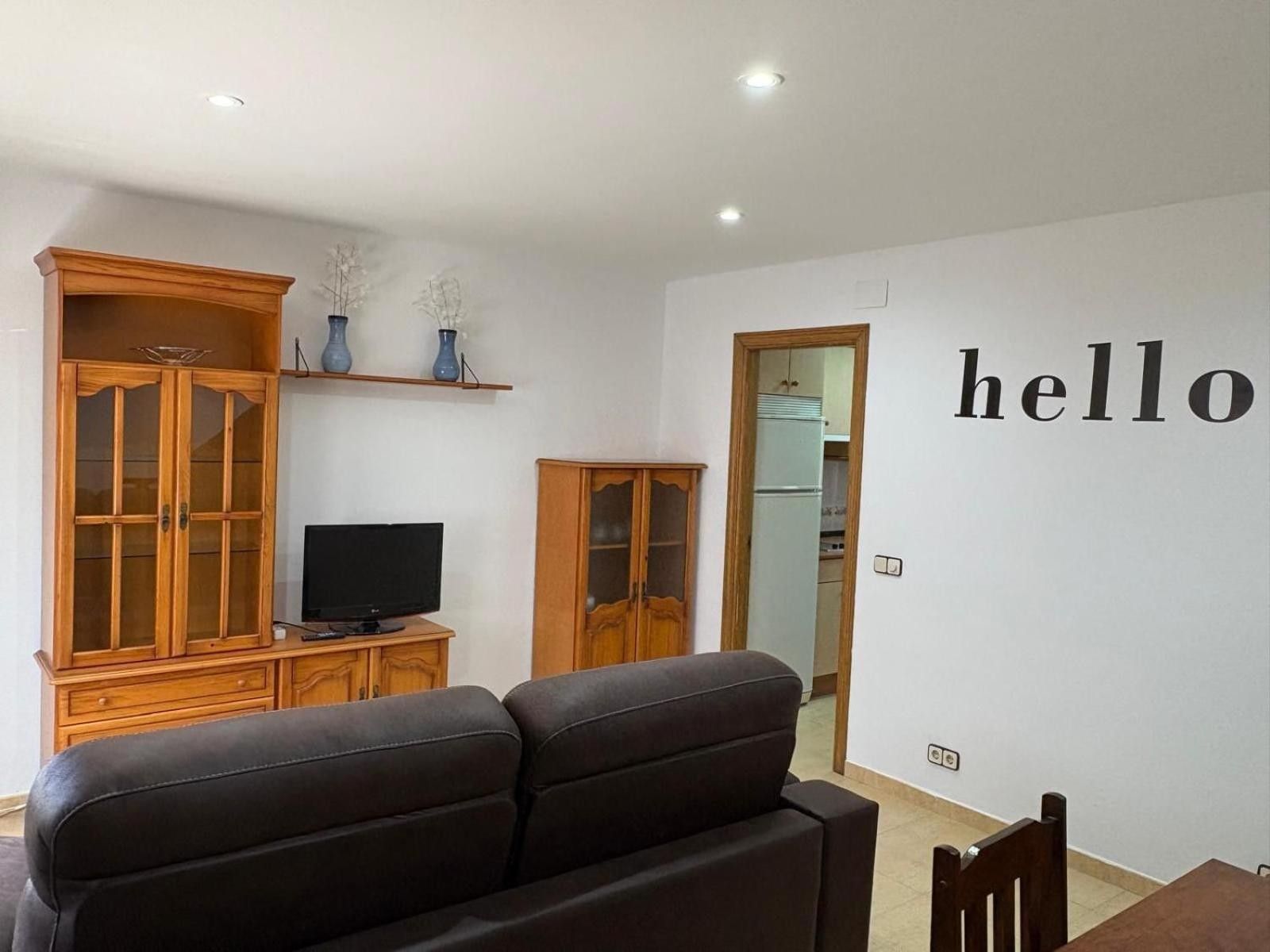 A living room with a sofa, TV, wooden cabinets, and a 'hello' wall decoration.
