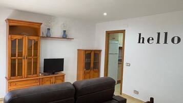 Ein Wohnzimmer mit einer Couch, einem Fernseher, Holzschränken und einer Wanddekoration mit dem Schriftzug 'hello'.