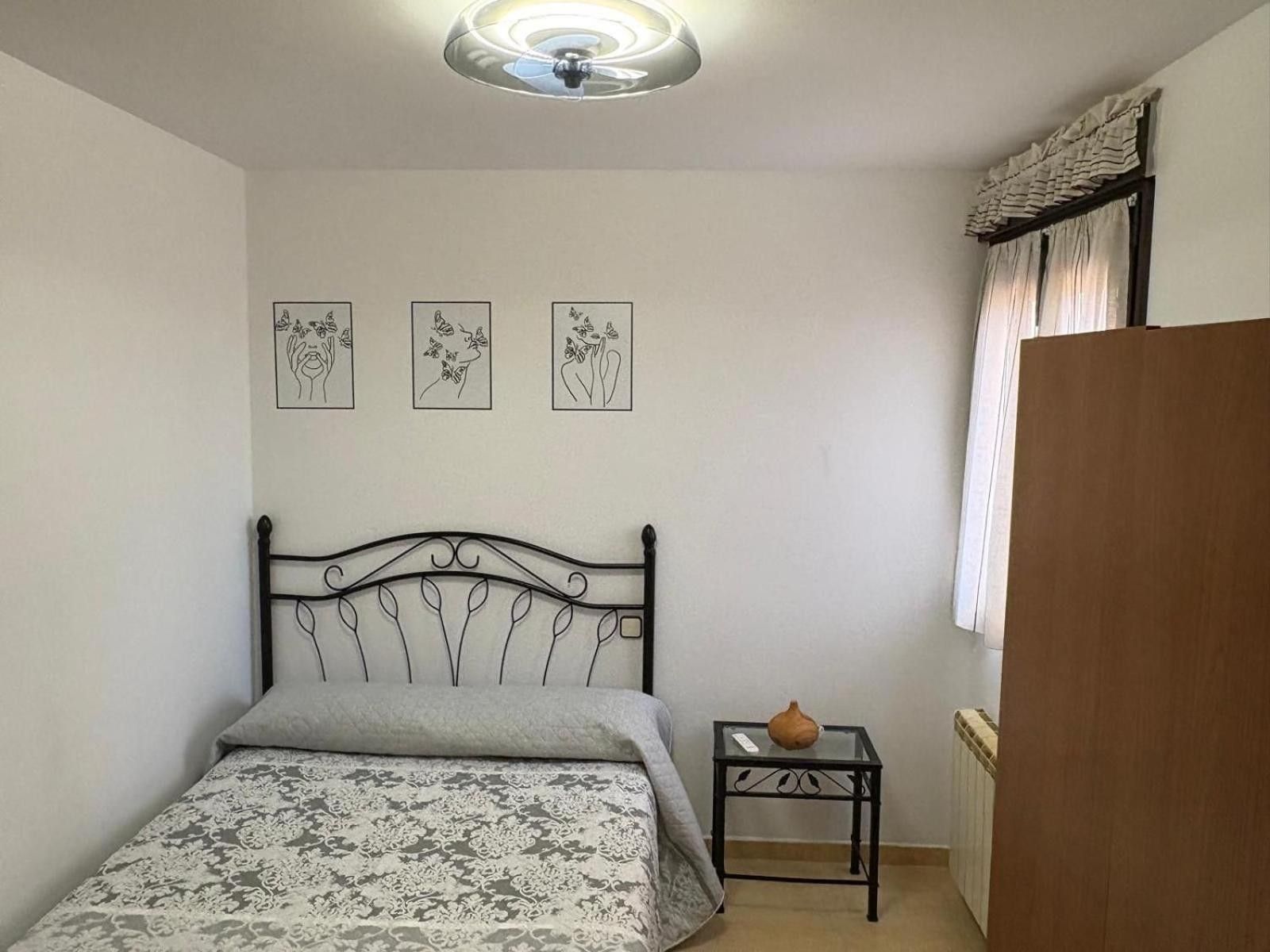 Un dormitorio con una cama, una mesita con un florero y tres cuadros colgados en la pared.