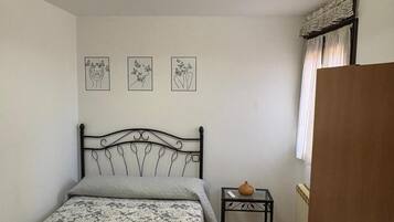 Un dormitorio con una cama, una mesita con un florero y tres cuadros colgados en la pared.