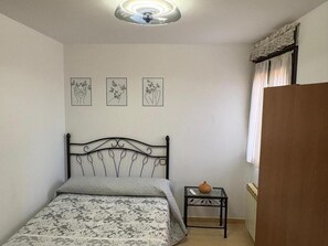 A bedroom with a bed, a small table with a vase, and three wall-mounted pictures.