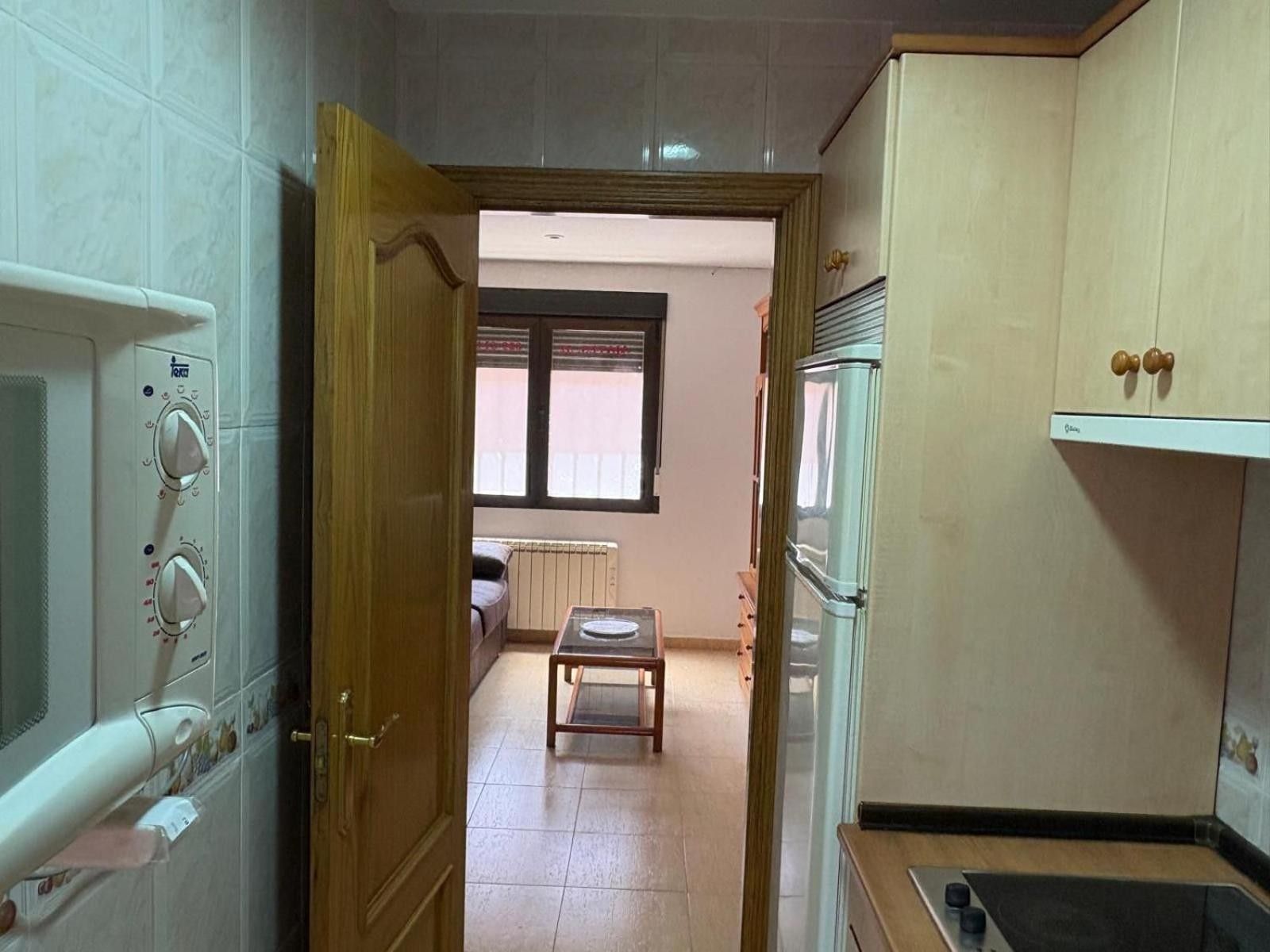 Cocina con microondas, horno y refrigerador. Se ve una ventana con persianas y un radiador al fondo.