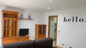 A living room with a sofa, TV, wooden cabinets, and a wall with the word 'hello'.