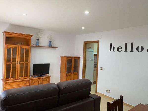 A living room with a sofa, TV, wooden cabinets, and a wall with the word 'hello'.