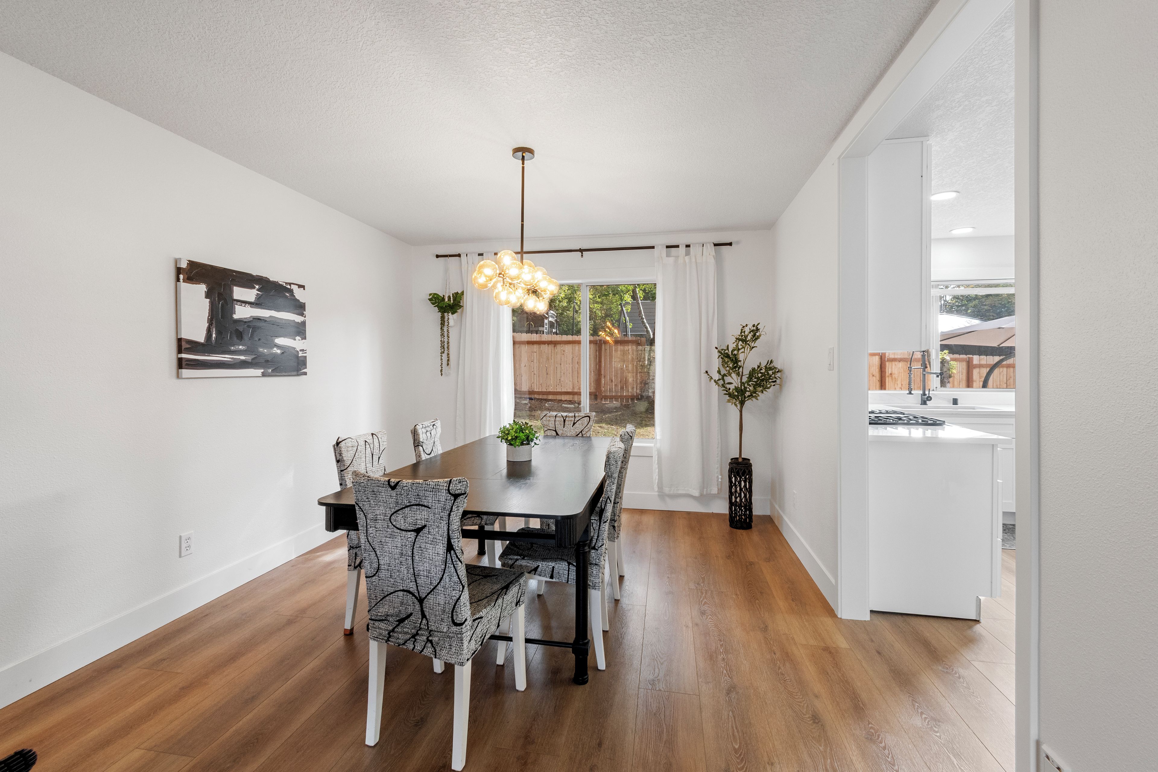 Un espace repas comprenant une table en bois, des chaises à motifs, un luminaire suspendu et une vue sur l’extérieur.