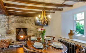 A dining area with a stone fireplace, wooden beams, a chandelier, and a table set for four. - Sleeps5-petfriendly-coalfire-snowdonia (Dolgellau)