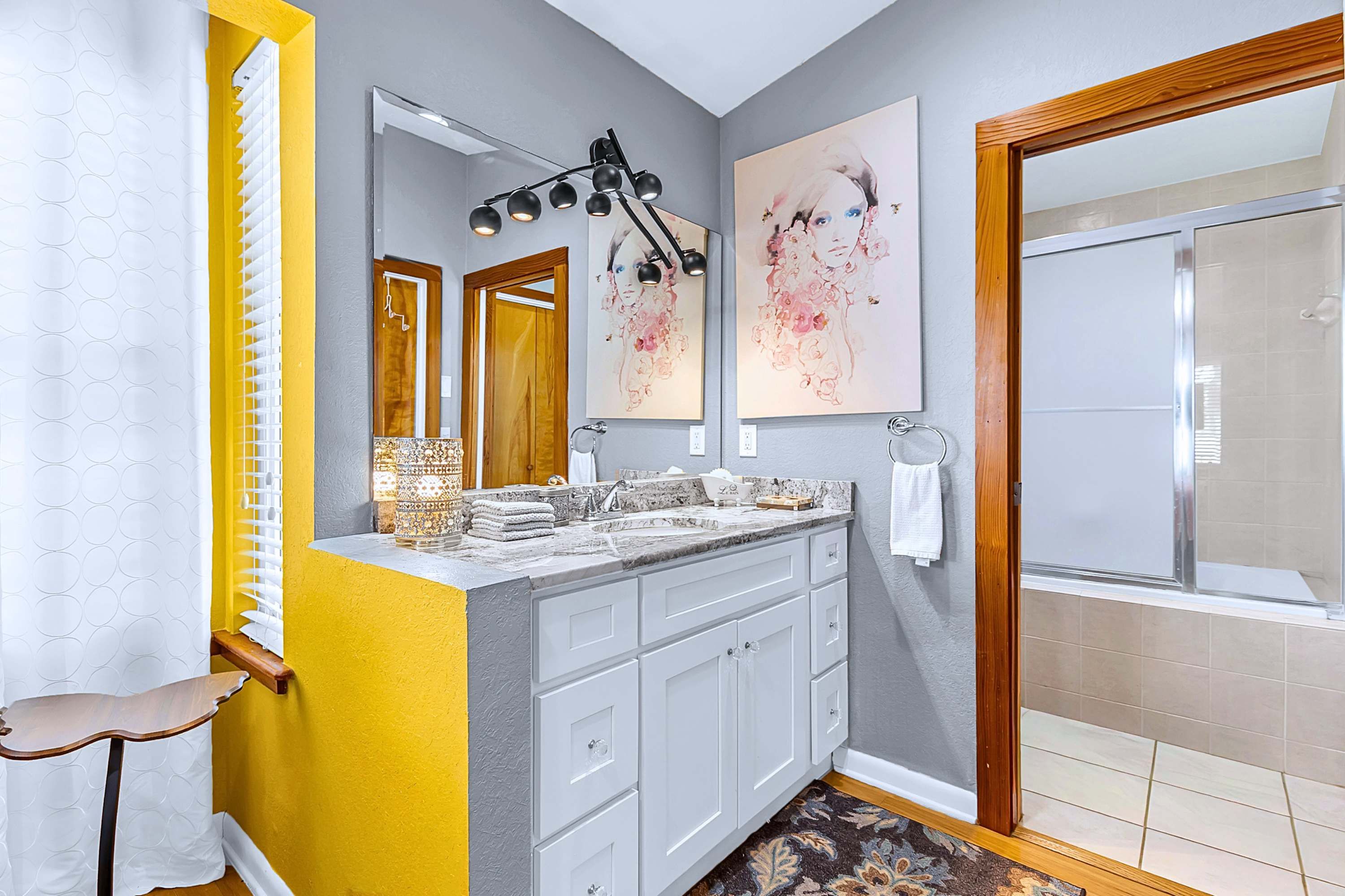 A bathroom with a double vanity, a large mirror, a shower, and two wall-mounted artworks.