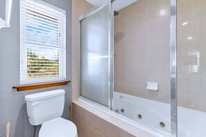 Un baño con inodoro, cabina de ducha y ventana con persianas.