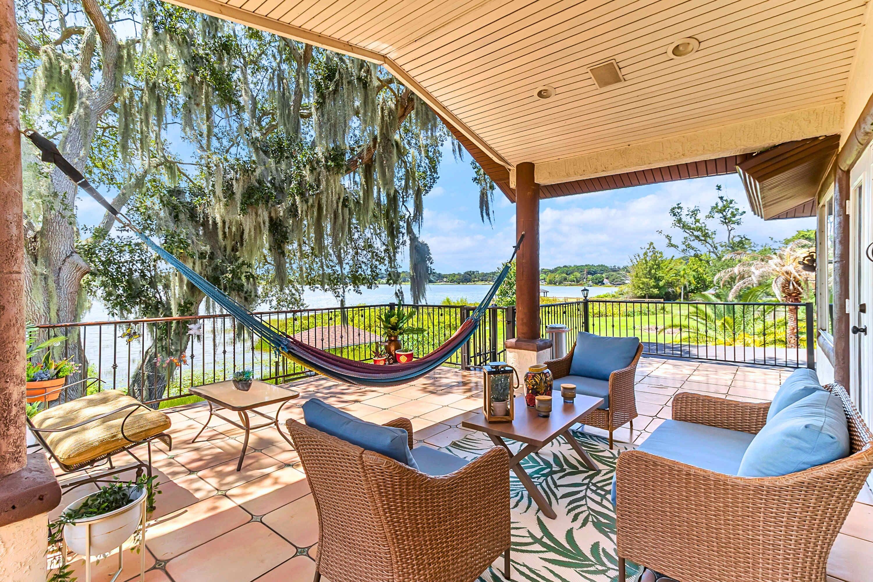 Un patio techado con mobiliario de mimbre, una hamaca y vista a un lago.
