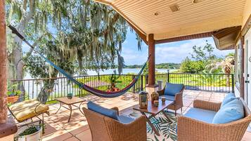 Un patio techado con mobiliario de mimbre, una hamaca y vista a un lago.