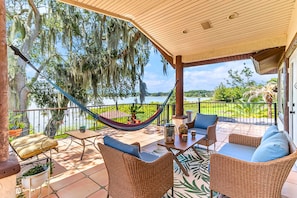 Un patio techado con mobiliario de mimbre, una hamaca y vista a un lago.