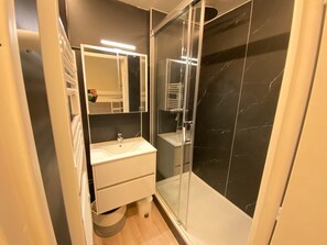 Ein modernes Badezimmer mit einer gläsernen Dusche, einem weißen Waschbecken und einem Spiegel darüber.