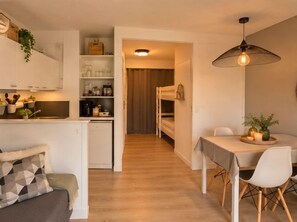 Ein kleiner Wohnbereich mit Küchenzeile, Essbereich und einem Hochbett im Hintergrund.