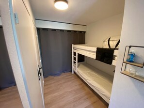 Ein Schlafzimmer mit Etagenbetten, einer Deckenleuchte, einem Regal mit einer Wasserflasche und einem Vorhang.