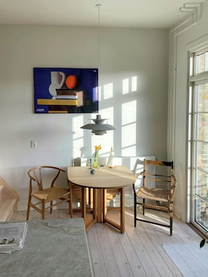 A dining area with a round table, two chairs, a hanging light fixture, and a painting on the wall. - Two-floor flat with balcony in Vesterbro (København V)