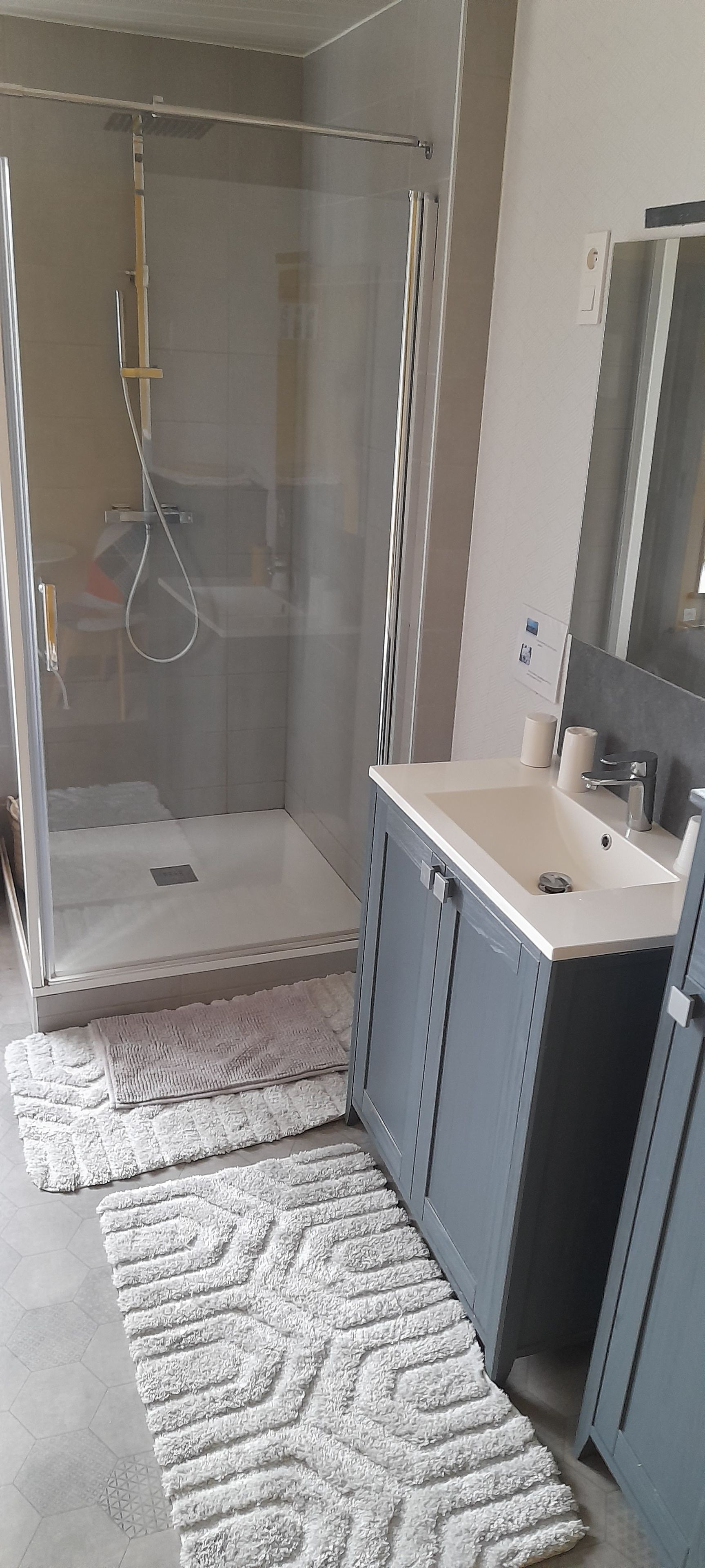 Une salle de bain moderne avec une douche à parois de verre, un lavabo avec un miroir et un tapis à motifs sur le sol.