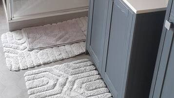 Une salle de bain moderne avec une douche à parois de verre, un lavabo avec un miroir et un tapis à motifs sur le sol.