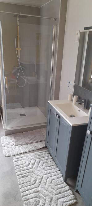 Een moderne badkamer met een douchecabine van glas, een wastafel met spiegel en een geruwd vloerkleed.