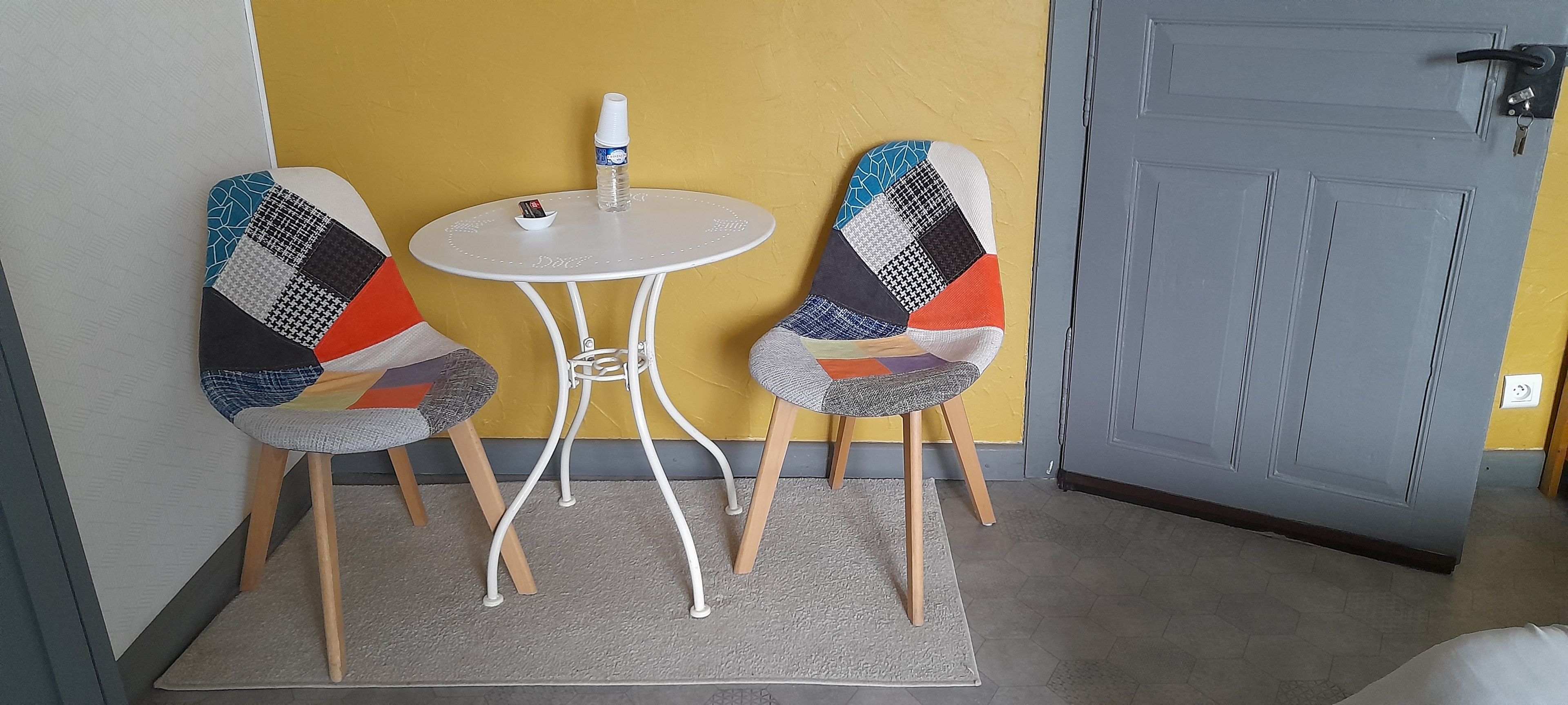 Een kleine kamer met twee stoelen, een tafel en een deur.