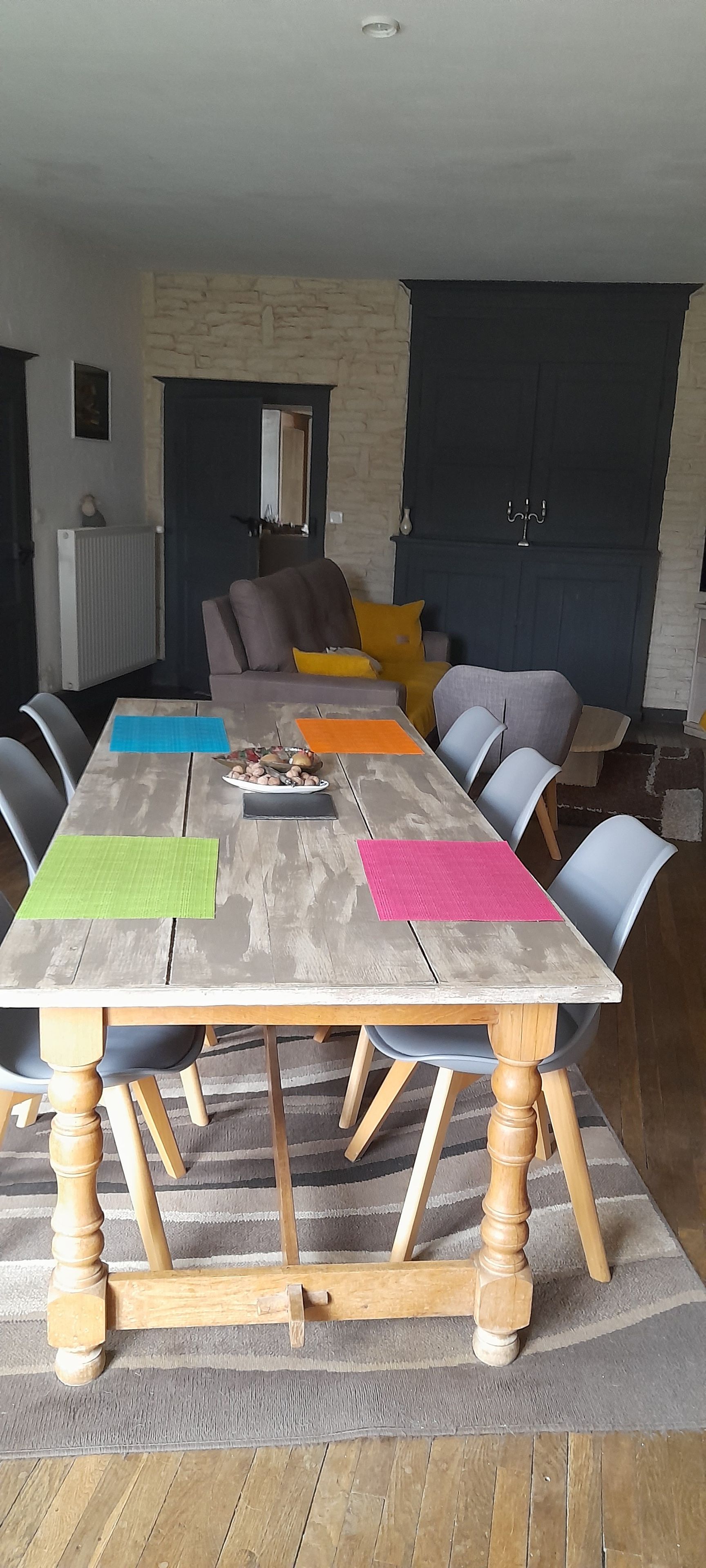 Un espace repas avec une grande table en bois, plusieurs chaises et un mur en pierre en arrière-plan.