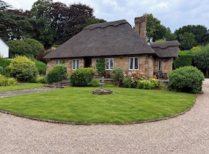 A stone house with a thatched roof, surrounded by a well-maintained lawn and a gravel driveway. - Tudor Lodge (Belper)