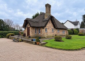 A stone cottage with a thatched roof, a chimney, and a gravel driveway. - Tudor Lodge (Belper)