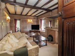 A traditional living room with a sofa, a television, a fireplace, and wooden beams on the ceiling. - Tudor Lodge (Belper)