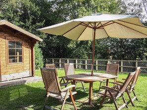 A wooden deck with a table and chairs, an umbrella, and a wooden building in the background. - Tudor Lodge (Belper)
