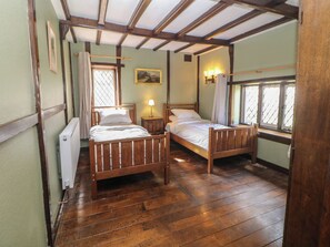 A room with two wooden beds, a radiator, a window with curtains, and a painting on the wall. - Tudor Lodge (Belper)