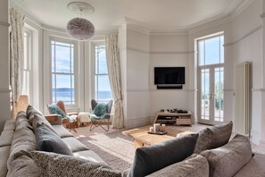 A spacious living room with a large sofa, a coffee table, and a television mounted on the wall. - Memory House (Woolacombe)