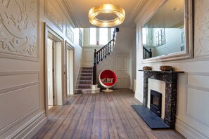 A hallway with a wooden floor, a staircase with a red chair, and a fireplace. - Memory House (Woolacombe)