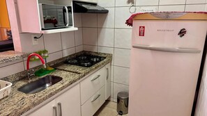 Una cocina con estufa a gas, un lavamanos, un microondas y un refrigerador.