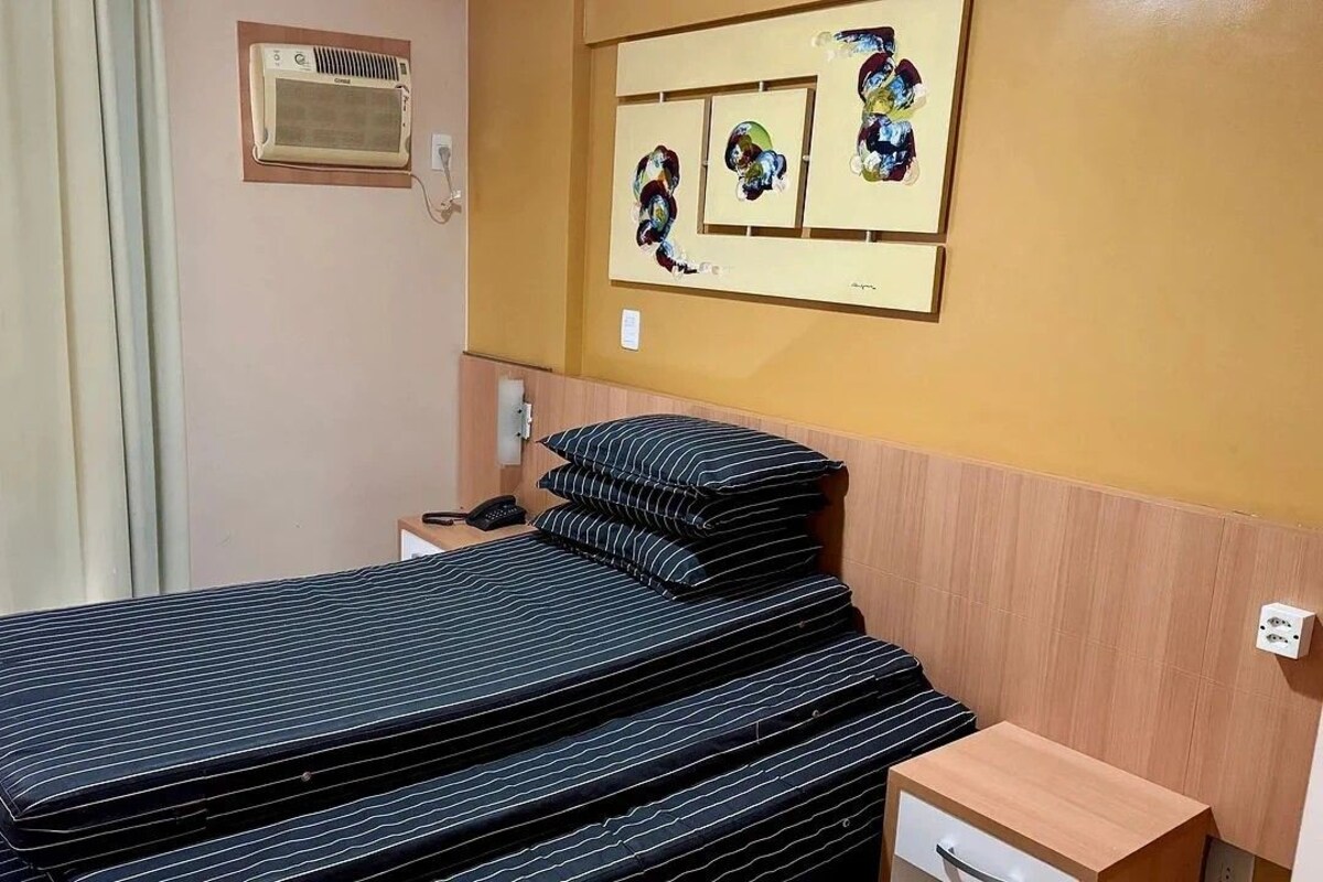 A hotel room with a bed, a bedside table, a mirror, and artwork on the wall.