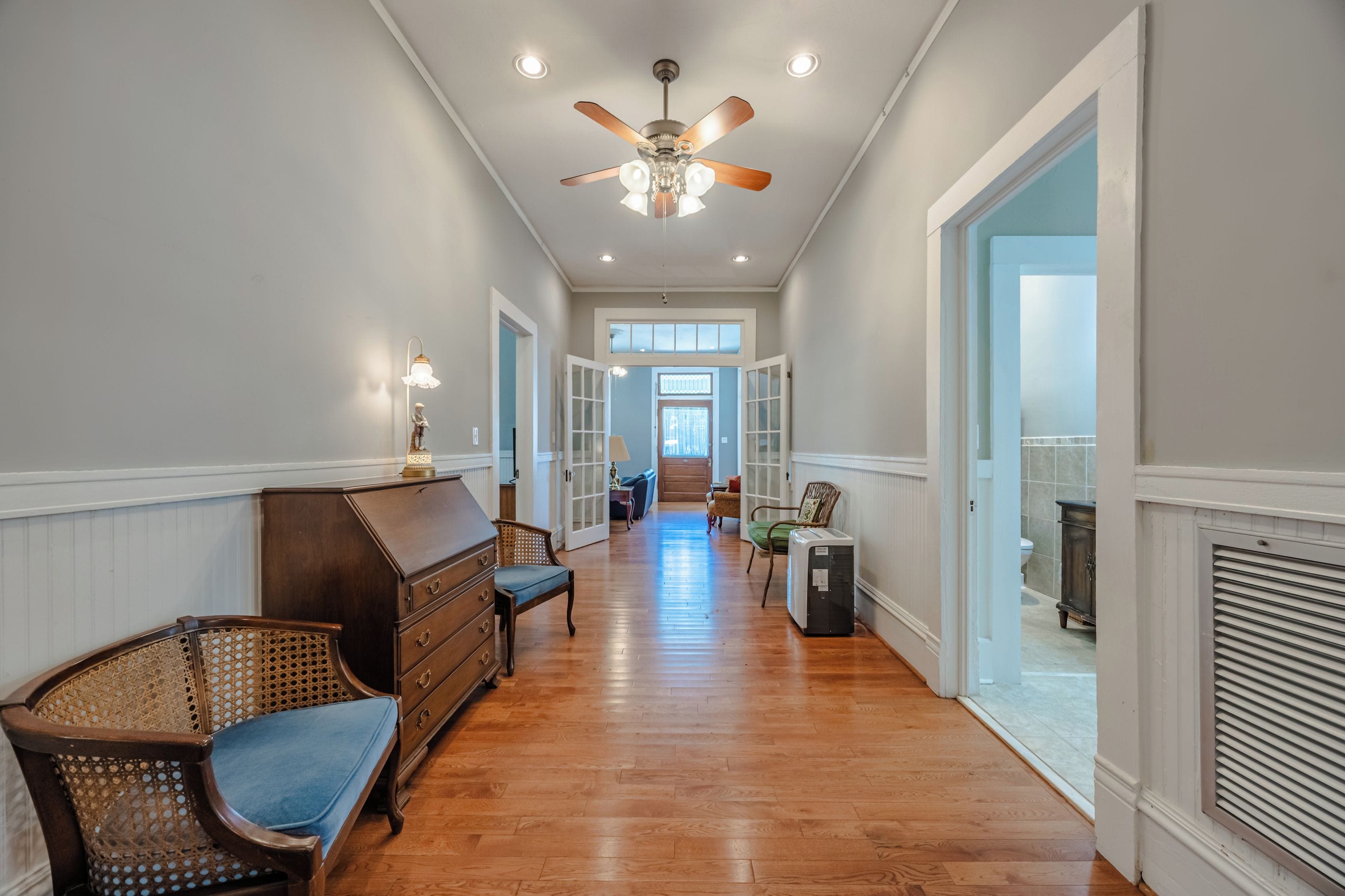 A hallway with a ceiling fan, wooden flooring, and a view into a room with a window.